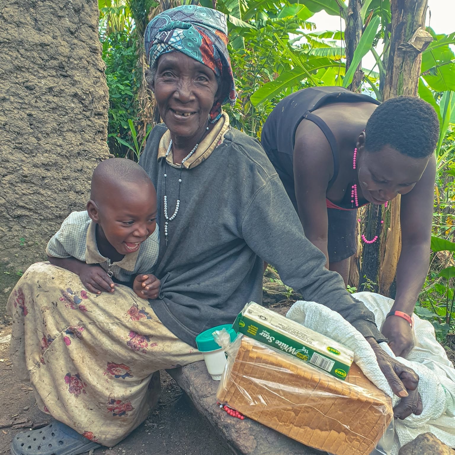 An elderly woman and a smiling child beside food provisions in rural Uganda